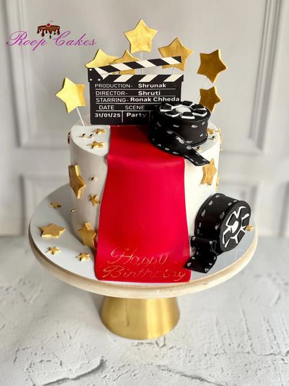 Lights, camera, action. This movie-themed cake is perfect for a film buff, featuring a red carpet, golden stars, a film reel, and a personalized clapperboard.