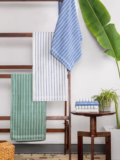 This shot styles the towels in a more dynamic, layered way on a wooden ladder. The addition of a large plant creates a fresh, natural, and stylish bathroom or home environment.