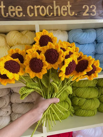 Holding up a fresh bouquet of sunflower stems in front of my colorful yarn shelf.
