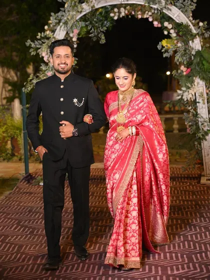 The couple making their entrance at the reception, the bride looking stunning in a pink saree and the groom sharp in a black bandhgala.