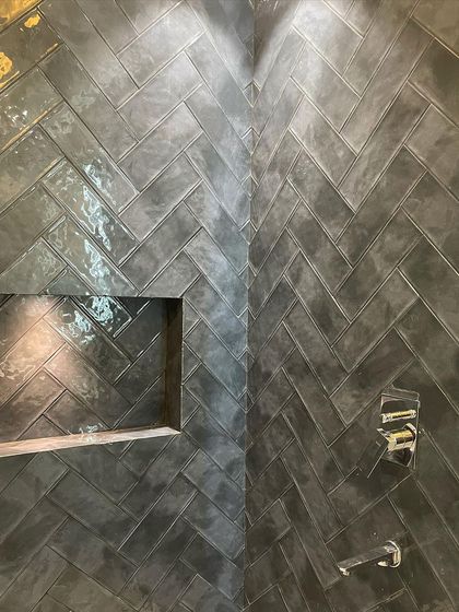 A detailed close-up of the herringbone tilework inside the shower, showing the built-in niche for shampoo and soap.