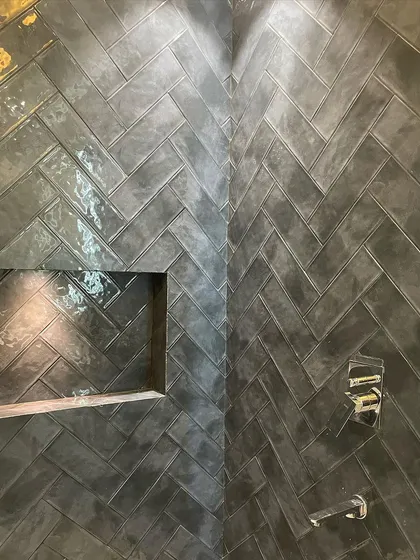 A detailed close-up of the herringbone tilework inside the shower, showing the built-in niche for shampoo and soap.