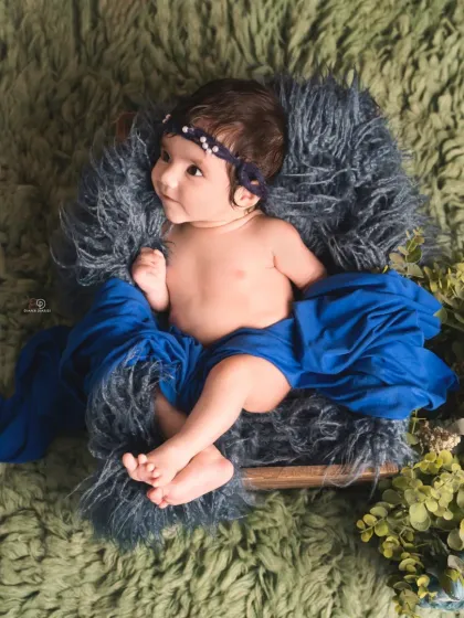A beautiful color combination of royal blue and green makes this baby portrait pop. The baby is propped up in a basket, looking off to the side with a curious expression.