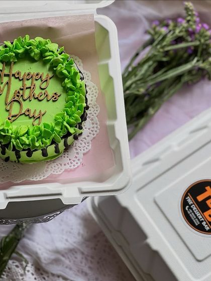 This vibrant green Mother's Day bento cake features a chocolate drip and a wooden topper. Each one is packed in its own box, ready for gifting.