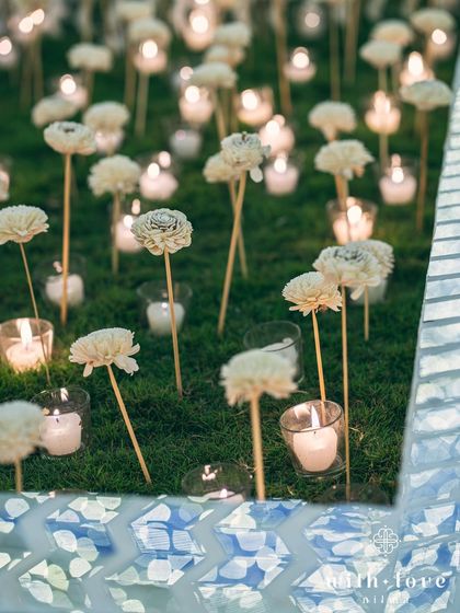 A field of delicate paper flowers and candles creates a magical pathway. This installation, set against a blue and white Thikri mosaic border, adds a soft, romantic touch to the grand sangeet decor.