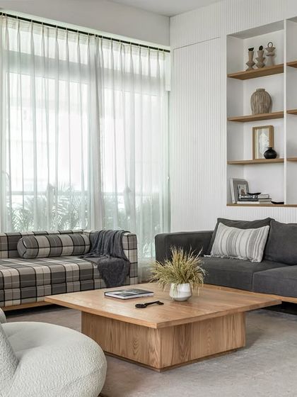 A modern farmhouse aesthetic defines this living room. The space blends natural elements like a fluted wall with built-in oak shelves, a comfortable grey sofa, and low-height white boucle chairs to encourage intimate conversations.