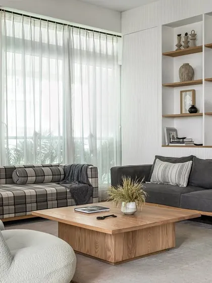 A modern farmhouse aesthetic defines this living room. The space blends natural elements like a fluted wall with built-in oak shelves, a comfortable grey sofa, and low-height white boucle chairs to encourage intimate conversations.
