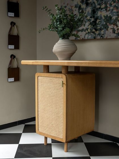 A close-up of a custom-designed desk from our furniture line, House of Goya. The piece features a light wood finish with a caned cabinet door, showcasing our commitment to craftsmanship and timeless materials.