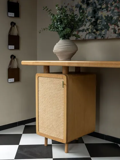 A detail of a custom-designed desk with a light oak finish and a cane-fronted cabinet. The clean lines and natural materials make it a beautiful and functional piece for a home office.