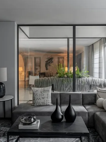 Glass partitions and an open layout create a sense of flow in this living area. A plush sectional sofa is arranged around a central planter, bringing a touch of nature indoors.