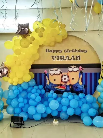 A Minions birthday setup with a custom backdrop and a balloon arch in blue and yellow, perfect for fans of the characters.