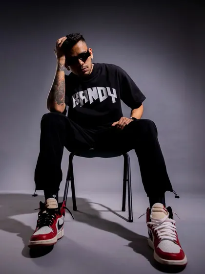 A seated pose that conveys a relaxed, confident attitude. The lighting highlights the model's sneakers and the logo on the t-shirt, focusing on key brand elements.