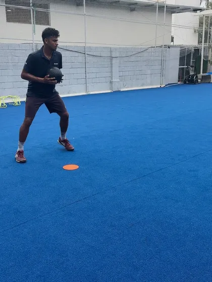An athlete preparing for a lateral shuffle drill with a medicine ball. This starting position emphasizes a low center of gravity and readiness, key for explosive side-to-side movement on the tennis court.