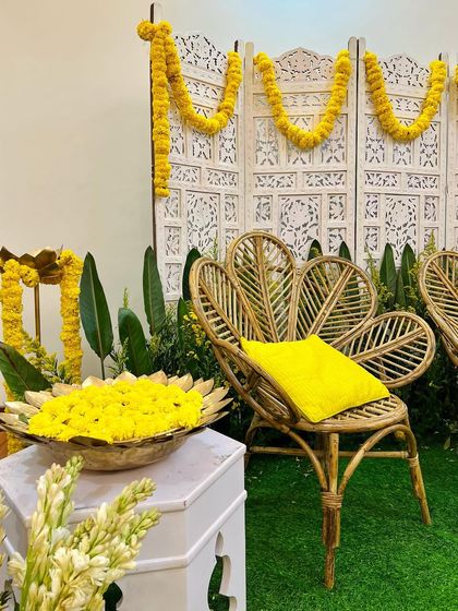 A simple and elegant setup for a festive occasion. The combination of cane furniture, marigold garlands, and brass elements creates a look that is both traditional and chic.