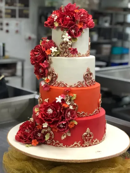 The completed four-tier custom cake for a mehendi function. The rich colors, detailed gold patterns, and handmade red sugar flowers came together to create a piece that was both traditional and stunning.
