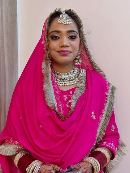 A direct portrait showcasing a beautiful Sikh bride. The look features a dramatic winged eyeliner and a custom lip color, paired with a maang tikka and traditional jewelry for a complete bridal ensemble.