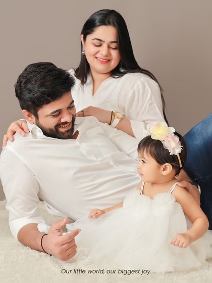 A relaxed family portrait on a soft white rug. The parents look on lovingly as their little one explores, creating a natural and heartwarming scene.