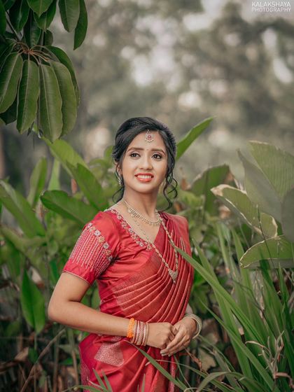 A candid portrait of a bride in a vibrant red saree, captured in a natural outdoor setting.