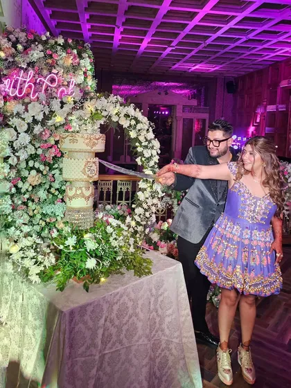 A happy couple cutting their white and gold chandelier cake at their post-wedding party.