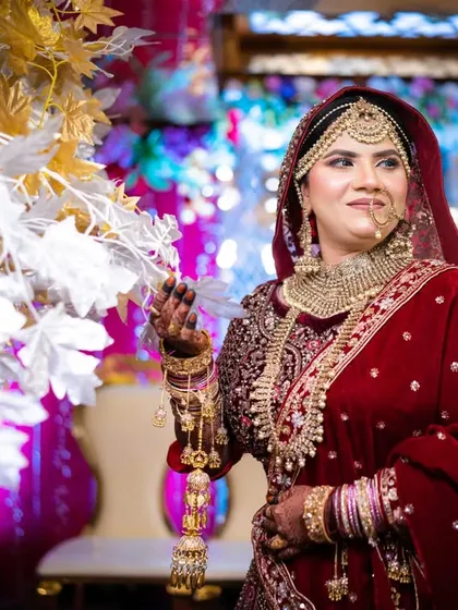 The bride posing with the floral decor, her rich velvet lehenga and intricate jewelry shining in the colorful lights.