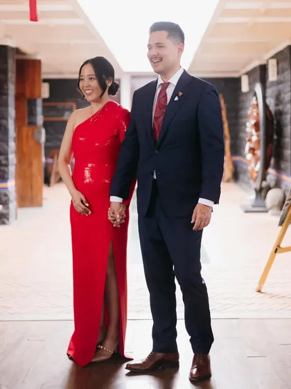 A stylish couple, with the bride in a vibrant red dress and the groom in a sharp suit, ready for their fusion wedding celebration.