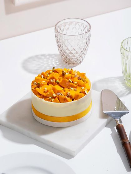 A close-up of a mango cake, showing the detail of the white chocolate collar and fresh fruit topping.