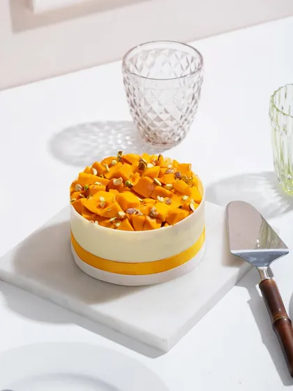 A close-up of a mango cake, showing the detail of the white chocolate collar and fresh fruit topping.