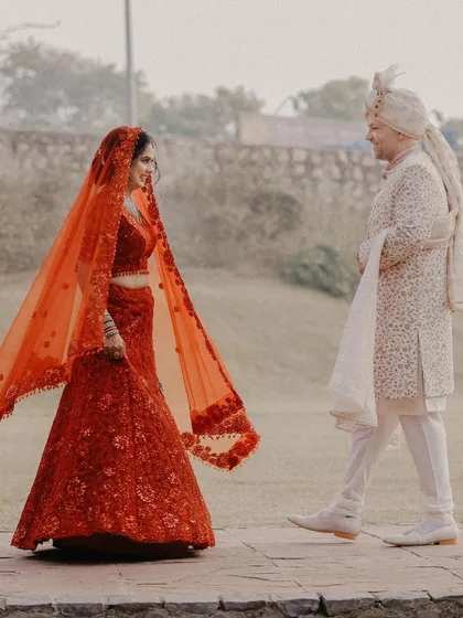 The "first look." A beautiful, candid moment as the groom sees his bride in her stunning red lehenga for the first time on their wedding day.