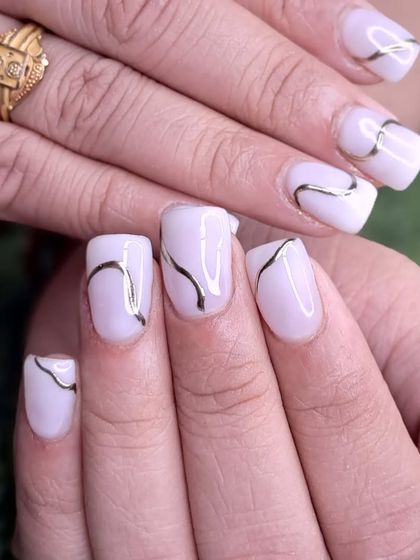 A beautiful set of short, square nails with a milky white base and elegant gold line art.