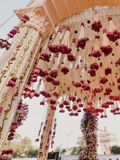 A close-up of the mandap ceiling, adorned with a dense canopy of red roses and lotus buds, with the Gateway of India visible in the distance.