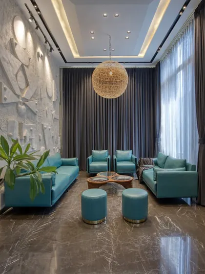 A formal drawing room with teal leather sofas set against a custom-designed, three-dimensional geometric art wall. A large rattan pendant light adds a touch of organic texture.