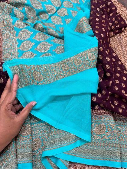 The plain wine-purple blouse piece for the turquoise Kadi georgette saree, with its simple woven border.