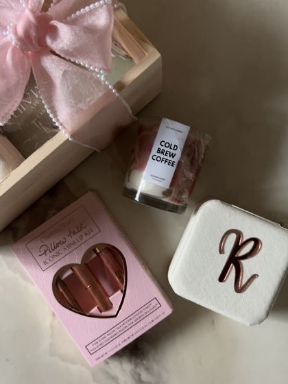 A close-up of some of the personalized items in a bridesmaid hamper, including a custom initial jewelry case and a coffee-scented candle.