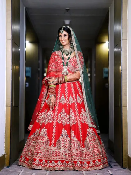 The bride looking radiant and confident in a hallway portrait. This shot highlights the stunning embroidery of her red and green lehenga.