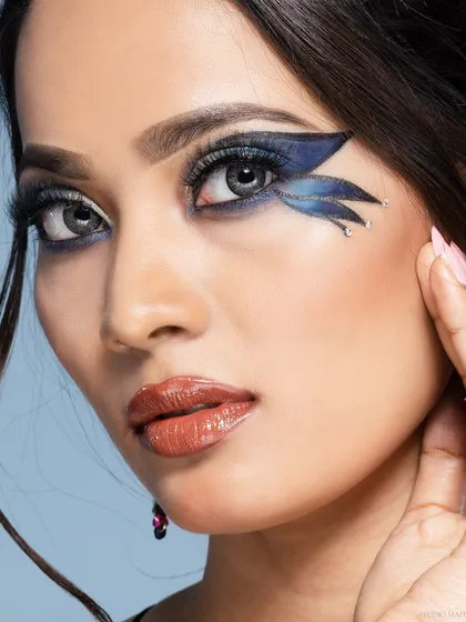 A creative beauty portrait with dramatic, wing-shaped eye makeup. The close-up highlights the makeup artist's skill and the model's striking features.