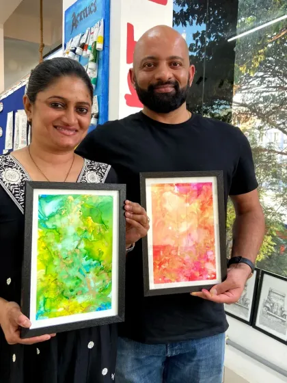 A couple proudly displays their framed alcohol ink paintings. This fluid art form allows you to create vibrant, abstract designs with stunning color blends.