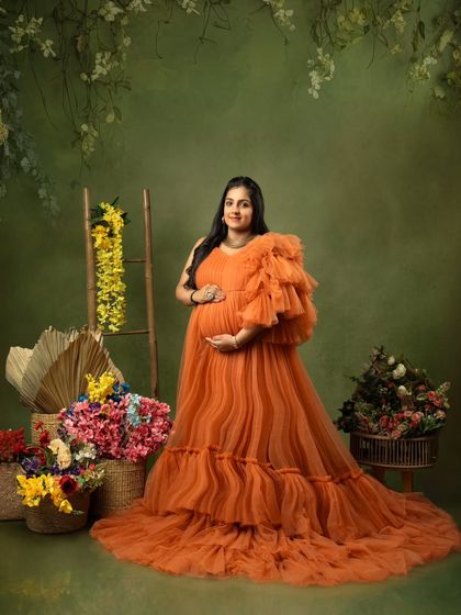 A joyful portrait of an expecting mother in a bright orange gown, surrounded by baskets of flowers.