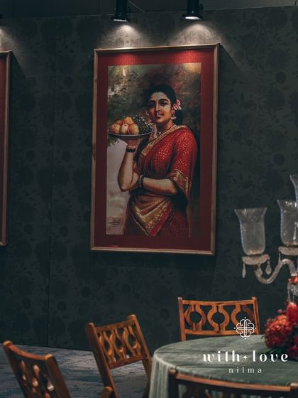 A cozy corner for conversation, with a Raja Ravi Varma painting taking center stage. The decor is designed to complement the art, with classic furniture and rich, dark colors.