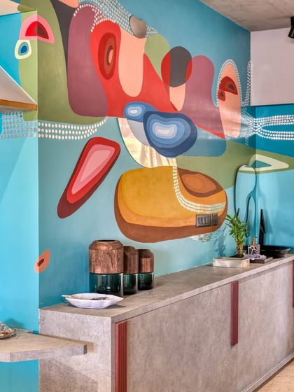 An abstract mural of 'pebbles and ripples,' featuring organic shapes and a vibrant color palette in a residential dining area.