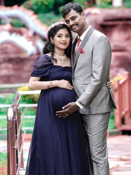 A formal and elegant couple's portrait. The coordinated outfits and classic pose by the railing result in a sophisticated and timeless image celebrating their pregnancy.