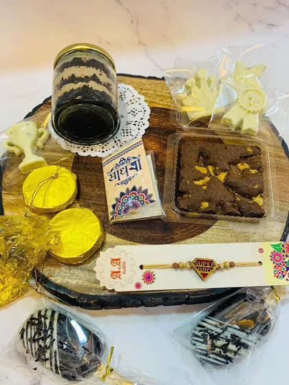 Here are the contents of the Rakhi hamper displayed, showing the variety of treats you get. The hamper includes double chocolate cakesicles, a jar cake, Rasmalai chocolates, dry fruit mendiants, a brownie, and a rakhi with traditional accompaniments.