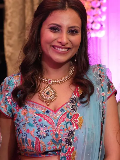 A close-up of the client's wedding guest look, highlighting her radiant smile and the perfect pairing of the outfit with the traditional gold jewelry.