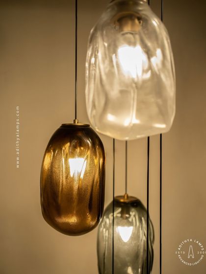 This cascading installation features pendants made of organic, free-form glass in smoked and amber tones. The textured, irregular shapes create a beautiful, water-like effect, perfect for adding a sense of calm and artistry to a room.