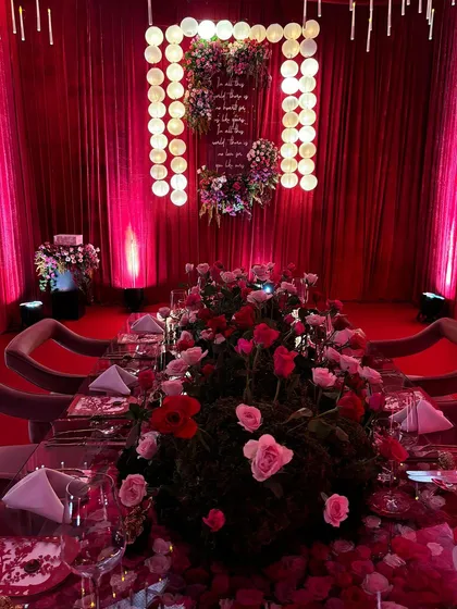 A dramatic, red-themed tablescape with Japanese-inspired elements. The centerpiece of moss and roses sits on a mirrored table, reflecting the moody lighting and creating an atmosphere of intense romance and sophistication.