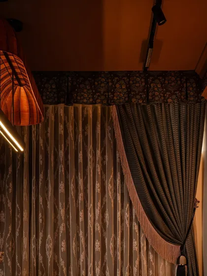 The lighting in Zone Three was designed to be as dramatic as the decor. A custom fabric-wrapped chandelier hangs above the client table, complemented by modern track lighting and layered, floor-to-ceiling drapes that add a theatrical touch.
