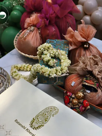 A beautiful flat lay of traditional elements from a Godhbarai ceremony. It includes a custom invitation, fragrant jasmine garlands, and beautifully wrapped gift potlis, all styled to reflect a blend of tradition and elegance.