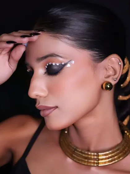 A side profile of the Egyptian-inspired makeup, highlighting the sharp, graphic eyeliner and the golden accessories in the hair.