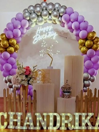 This elegant setup is perfect for milestone birthdays. It features a purple, gold, and silver balloon arch, my 'Happy Birthday' neon sign, and custom light-up marquee letters, all framed by a small picket fence for a finished look.