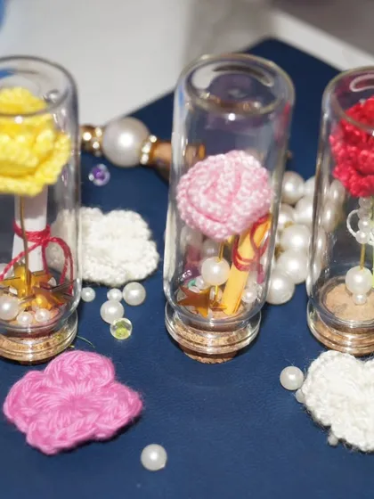An assortment of my 'message in a bottle' creations, with roses in yellow, pink, and red, surrounded by loose pearls and crochet hearts.