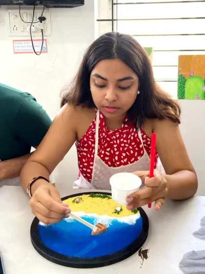A participant carefully adds details to her resin beach art, placing a tiny boat on the shore. It’s these small, personal touches that make each piece unique.
